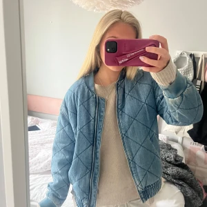Denim bomberjacka - Säljer en snygg blå quiltad bomberjacka med dragkedja. Jackan har en normal passform och långa ärmar. Perfekt för höst och vår!