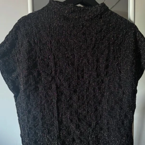 Svart glittrig topp - Säljer en svart glittrig topp med korta ärmar. Perfekt för att lysa upp vilken outfit som helst. Toppen har en elegant och festlig känsla, idealisk för speciella tillfällen.