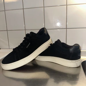 Svarta sneakers från Gant - Snygga svarta sneakers från Gant med vit sula och klassisk snörning. Skorna har en stilren design med Gant-logga på sidan och en röd sula undertill. Perfekta för en avslappnad stil. Använda 5-7 gånger 