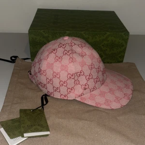 Rosa keps från Gucci - Snygg rosa keps från Gucci med det ikoniska GG-mönstret. Kepsen har en justerbar rem baktill och är tillverkad i ett slitstarkt material. Perfekt för att ge din outfit en lyxig touch.
