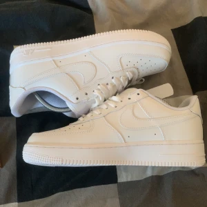 Vita Nike Air Force sneakers - Säljer ett par klassiska vita Nike Air Force sneakers. Dessa skor har en stilren design med snörning och perforerade detaljer på ovansidan för bättre ventilation. Perfekta för en avslappnad och trendig look.