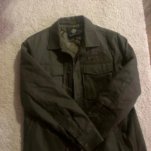 Grön jacka från Henri Lloyd - Säljer en stilren grön jacka från Henri Lloyd. Jackan har långa ärmar och knappar framtill samt två bröstfickor med knappar. Perfekt för en avslappnad stil.