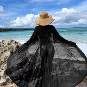 Svart strandklänning - Elegant svart strandklänning i transparent material med knytning i midjan. Långärmad design med volangdetaljer vid ärmslut. Perfekt för en dag på stranden eller vid poolen. Använd 1-2 gånger. 