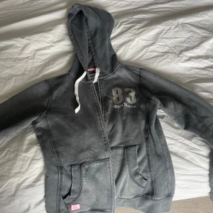 Grå hoodie från Race Marine - Mysig grå hoodie från Race Marine med broderad logga och siffran 83 på bröstet. Tröjan har huva med vita snören, dragkedja framtill och två stora fickor. Insidan är fodrad i mjuk fleece.