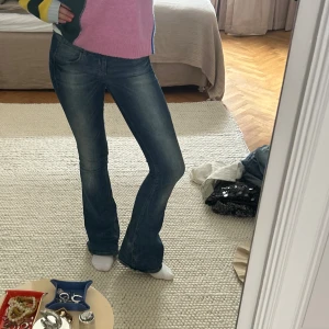 Blå bootcut jeans med låg midja - Säljer ett par snygga blå jeans med bootcut-modell och låg midja. Jeansen har klassisk femficksdesign, lätt slitning och är i stretchigt denim som sitter tajt upptill och släpper ut vid benslutet. Perfekta för dig som gillar en retro vibe.