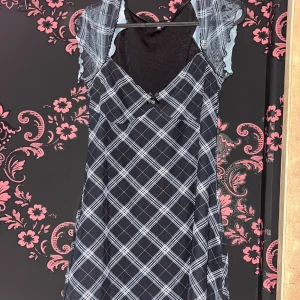 Rutig svart och vit kortklänning - Supersöt kortklänning med svartvitt rutmönster och transparenta volangärmar. Klänningen har v-ringning med liten rosett framtill och är figurnära upptill. Perfekt för dig som gillar en edgy men söt stil.