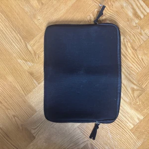 Svart datorväska från Kungsbacka - En stilren svart datorväska från Kungsbacka i mjukt neoprenmaterial. Väskan har en enkel, fyrkantig form och stängs med dragkedja. Perfekt för att skydda din laptop eller surfplatta när du är på språng.