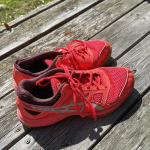 Rosa Asics Gel-Flare sneakers strl 40 - Snygga röda Asics Gel-Flare sneakers med silvriga detaljer och brun sula. Ovandelen är i mesh och syntet för bra andningsförmåga. Skorna har snörning och en sportig vibe, perfekta för dig som gillar färg och stil på gymmet eller ute.