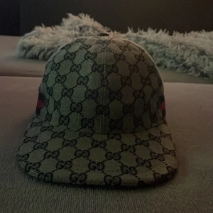 Gucci keps med GG-mönster, storlek M - Snygg keps från Gucci med klassiskt GG-monogram i mörkblått på beige bakgrund. Kepsen har justerbar rem bak i mörkblått skinn.          Priset kan diskuteras