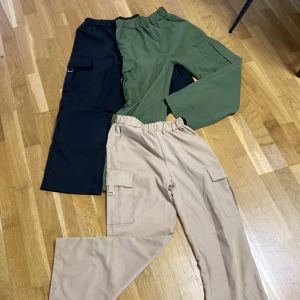 3 olika  cargopants i olika färger. Läs beskrivningen - Kontakta mig innan du köper vilken färg/hur många du vill ha.  Säljer tre par cargopants med elastisk midja och stora fickor på sidorna. Ett par är svarta, ett par är olivgröna och ett par är beige. Perfekta för en chill och avslappnad stil. Materialet känns som bomull eller polyester och byxorna har raka ben. 1 för 20kr. 2 för 35kr. Alla 3 för 45kr.