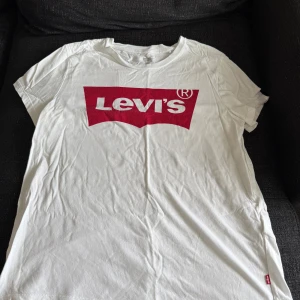 Vit Levi's t-shirt med röd logga - Vit t-shirt från Levi's med klassisk röd logga framtill. T-shirten har rund halsringning och korta ärmar. Tillverkad i mjuk bomull som känns skön mot huden. Perfekt för en avslappnad och stilren look.