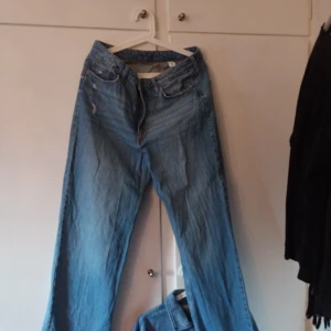Blå wide jeans med slitningar - Säljer ett par ljusblå jeans med breda ben och snygga slitningar vid fickan. Klassisk femficksmodell med dragkedja och bälteshällor. Perfekta för en avslappnad och trendig look.