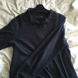 Mörkblå pikétröja från 157 - Säljer en stilren mörkblå pikétröja från 157 i storlek M. Tröjan har klassisk krage och knäppning framtill samt långa ärmar. Perfekt för dig som gillar en enkel och clean look.