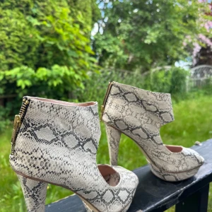 Ormskinnsmönstrade klackskor med dragkedja - Snygga pumps med ormskinnsmönster i beige och svart. Skorna har hög klack, plattform och öppen tå. Dragkedja baktill för enkel påtagning. Perfekta för dig som vill sticka ut med ett djurmönstrat statement. Skorna är vintage.