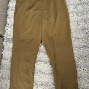 Beiga kostymbyxor från Ellos, strl 44 - Stilrena beiga kostymbyxor från Ellos i storlek 44. Byxorna har hög midja och rak passform, tillverkade i en mjuk mix av polyester och viskos. Perfekta för en clean och klassisk look.