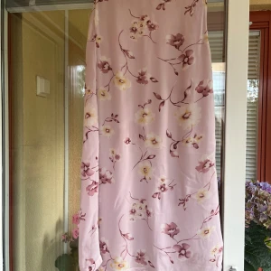 Ljusrosa blommig långkjol Flash - Superfin långkjol från Flash i ljusrosa med blommigt mönster i vinröda och gula toner. Kjolen har en rak och luftig passform, perfekt för varma dagar. Materialet är  lätt och svalt. Storlek M men känns som S. En mindre lagning (se sista bilden). 