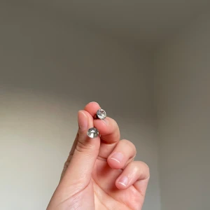 Silvriga örhängen med stora stenar - Ett par stilrena örhängen med stora, runda klara stenar i silverfärgad infattning. Perfekta för att ge lite extra bling till din look. Klassisk design som passar till det mesta och är lätta att bära hela dagen.