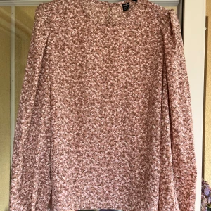 Rosa topp med mönster - Rosa topp i storlek 36 med små vita blommor. Läng ärm och en knapp bak. 