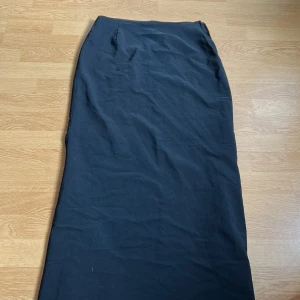 Svart långkjol från Vila - En stilren svart långkjol från Vila i klassisk rak modell. Kjolen har en diskret dragkedja i sidan för enkel på- och avtagning. Perfekt för dig som gillar minimalistisk och tidlös stil.