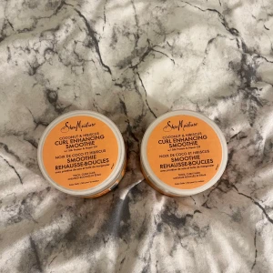 SheaMoisture Curl Enhancing Smoothie - Två burkar SheaMoisture Coconut & Hibiscus Curl Enhancing Smoothie, perfekt för lockigt och tjockt hår. Innehåller silkesprotein och neemolja. Kommer i runda plastburkar med orange etikett och genomskinligt lock, 340 g per burk. Luktar så gott, en av de har öppnats och använts nån gång! 