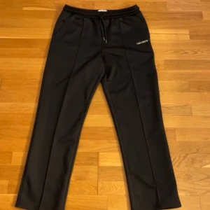 Svarta mjukisbyxor från Les Deux - Svarta mjukisbyxor från Les Deux med raka ben och diskret logga på ena sidan. Byxorna har dragsko i midjan och sidofickor. Snygg, enkel design som funkar till det mesta. Materialet känns mjukt och bekvämt.