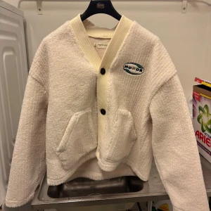 Vit teddyjacka från Honor The Gift - Supermjuk och oversized vit teddyjacka från Honor The Gift. Jackan har två stora fickor framtill, ribbad krage och knappstängning. Broderad logga på bröstet ger en clean och trendig vibe. Perfekt för dig som gillar en chill och cozy stil. Aldrig använd då jag fick den i present. Nypris 2000kr