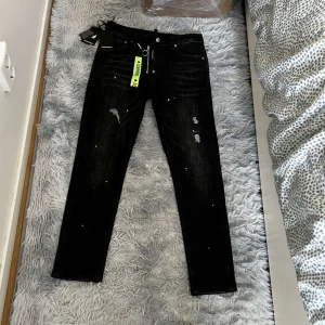 Svarta jeans från Dsquared2 - Säljer ett par svarta jeans från Dsquared2 med slitningar och färgstänk för en riktigt edgy look. Jeansen har raka ben, klassisk femficksmodell och coola detaljer som dragkedja med ring. Perfekta för dig som vill sticka ut. Helt nya med lapp o allt. 
