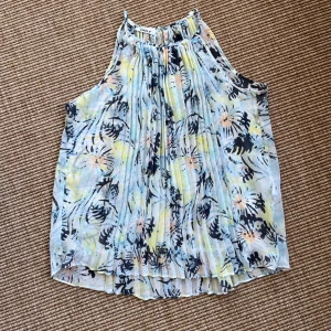 Blommig ärmlös topp från ONLY - Superfin ärmlös topp från ONLY i storlek 34. Toppen har ett blommigt mönster i ljusblått, gult, svart och lite rosa. Den är luftig och har plisserade detaljer som ger en luftig och lätt  känsla. 