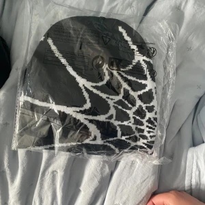 Svartvit stickad mössa med spindelnätsmönster - Cool svart mössa med vitt spindelnätsmönster, perfekt för dig som vill sticka ut. Stickad i mjukt material som håller dig varm och ger en edgy vibe till din outfit. Passar perfekt till höst och vinter.