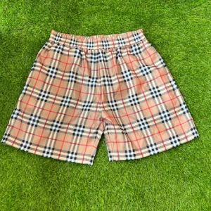 Rutig Burberry shorts i beige - Snygga shorts från Burberry i klassiskt beige rutigt mönster med röda och svarta detaljer. De har elastisk midja och meshfoder på insidan, perfekta för sommaren. Ikonisk design som sticker ut och känns lyxig.