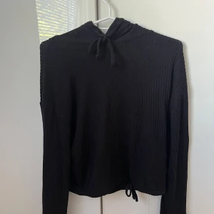Svart ribbad tunn kofta från Gina Tricot - Svart ribbad tunn hoodie från Gina Tricot i storlek S. Tröjan har långa ärmar, huva och snörning både vid halsen och nederkanten. Materialet är mjukt och stretchigt 