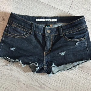 Mörkblå jeansshorts från MOTO - Snygga mörkblå jeansshorts från MOTO med slitna detaljer och fransig kant. Lågmidjade och kort i modellen. Oanvända då de är för stora i midjan. Köpta för 450