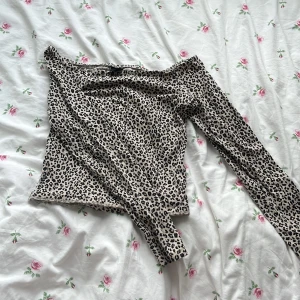 Leopardmönstrad offshoulder topp Gina Tricot - Säljer en snygg offshoulder topp från Gina Tricot i leopardmönster. Toppen är beige med svarta fläckar, har långa ärmar och sitter tight. 