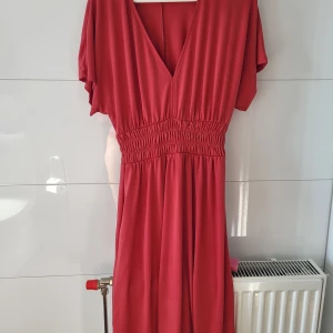 Mörk koral/ rosa v-ringad klänning från Zara - Superfin mörkkoral/rosa klänning från Zara med v-ringning och korta ärmar. Smockad midja som ger en snygg siluett och flowy kjol. Perfekt för dig som gillar en enkel men stilren look. Materialet känns mjukt och lätt.