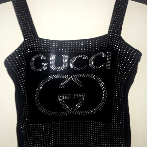 Svart glittrig topp med strass och logga - Två svarta linne-toppar med breda axelband, täckta av glittrande strass. framtill, båda i silverfärgade stenar. Snygg, iögonfallande och perfekt för dig som vill sticka ut med lyxig vibe.