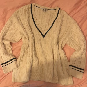 Beige kabelstickad tröja & Other Stories - Kabelstickad beige tröja från & Other Stories med djup v-ringning och svarta ränder vid halsringning och ärmslut. Oversized fit med långa ärmar och breda muddar. Perfekt för lager-på-lager och chill höst/vinterstil.