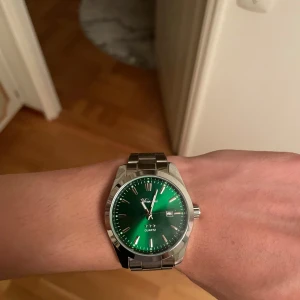 Grön klocka från Doventi med stållänk - Stilren klocka från Doventi med grön urtavla och silverfärgade index. Klockan har en robust länk i metall och datumvisning vid klockan tre. Klassisk rund boett i silverfärgat stål och quartz-urverk. Perfekt accessoar för dig som vill sticka ut med färg.