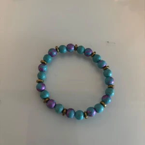 Turkost pärlarmband med lila detaljer - Färgglatt armband med turkosa pärlor och inslag av lila metallic. Mellan pärlorna sitter små guldfärgade ringar som ger extra bling. Perfekt accessoar för dig som vill sticka ut och addera färg till din stil. 
