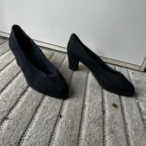 Svarta mockapumps från Rossini - Klassiska svarta pumps från Rossini i mocka med rund tå och stabil klack. Snygg och tidlös modell som passar till många olika outfits. Perfekta för dig som gillar en enkel men elegant stil.