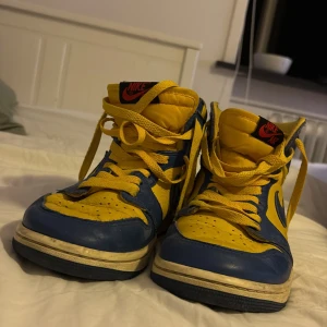 Nike Air Jordan 1 gul/blå sneakers - Nike Air Jordan 1 sneakers i en riktigt fet färgkombo av gult och blått. Klassisk high-top siluett med snörning, rund tå och vit sula. Skorna är i skinn och har ikoniska Air Jordan-loggan på sidan samt Nike Air-märke på plösen. Dom är lite smutsiga men det går att tvätt bort! Köpte dom för 1200