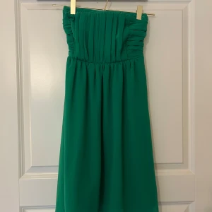 Grön kortklänning - Snygg grön klänning med plisserad överdel och smock i ryggen. Klänningen har en dragkedja i sidan. Tyvärr för liten för mig, och endast använd en gång. Perfekt för dig som vill sticka ut med färg och stil ❣️