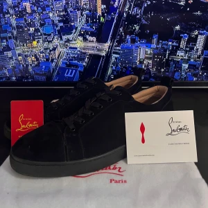 Christian Louboutins - Snygga svarta sneakers från Christian Louboutin i mocka med klassisk röd sula och svarta snören. Skorna har en stilren design med rund tå och platt sula, perfekt för dig som vill sticka ut med exklusiva detaljer. Kommer med originalpåse och certifikat.