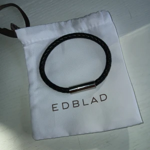 Svart flätat armband från Edblad - Stilrent svart armband från Edblad i flätat material med ett snyggt magnetlås i silverfärg. Perfekt accessoar för en clean look och passar både tjejer och killar. Levereras i originalpåse från Edblad.