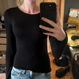 Svart långärmad topp Gina Tricot - En svart, tight långärmad topp från Gina Tricot i storlek XS. Enkel och stilren design med rund halsringning, perfekt att matcha med jeans eller kjol. Tillverkad i mjuk bomullsmix som sitter skönt mot kroppen.