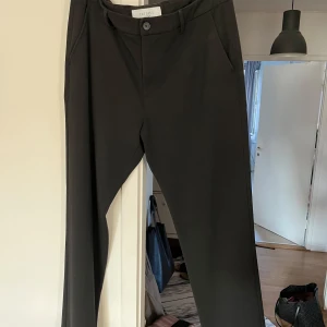 Svarta kostymbyxor från Les Deux - Stilrena svarta kostymbyxor från Les Deux med regular fit. Klassisk design med raka ben, bälteshällor och fickor fram och bak. Perfekta för en clean och dressad look. Materialet känns mjukt och har en snygg finish.