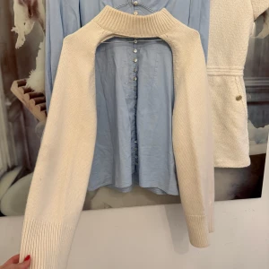 Stickad ärmtröja Nathalie Schuterman - Supercool stickad ärmtröja från Nathalie Schuterman i offwhite. Tröjan har bred ribbad krage och långa ärmar, perfekt att slänga över ett linne eller topp för en trendig lager-på-lager-look.