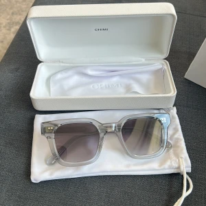 Transparenta solglasögon från CHIMI - Snygga solglasögon från CHIMI med transparent båge och fyrkantig form. Glasen är gråtonade och bågarna är i ett stilrent syntetmaterial. Kommer med originalfodral och putsduk. Perfekta för dig som vill ha en clean och modern look. Dessa är chimi 04 och pris kan diskuteras. 