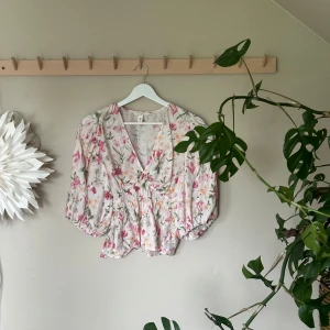 Blommig omlottblus med puffärm - Supersöt blommig blus från H&M i ljusrosa och vitt med gröna detaljer. Blusen har v-ringning, puffiga trekvartsärmar och smockad midja som ger en snygg siluett. Perfekt för vår och sommar när du vill känna dig extra fin.