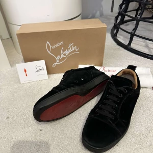 Svarta sneakers från Christian Louboutin - Snygga svarta sneakers från Christian Louboutin i mocka med klassisk röd sula. Skorna har rund tå, svarta snören och diskreta sömdetaljer. Insidan är beige och de har en lyxig känsla som sticker ut med den ikoniska röda undersidan.