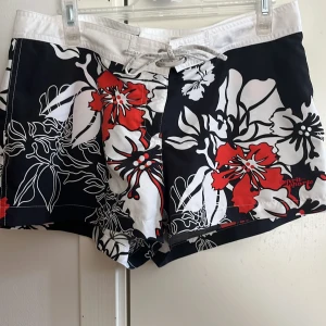 Blommiga surfshorts från Esprit Sports - Snygga surfshorts från Esprit Sports med stort blommönster i svart, vitt och orange. Shortsen har snörning i midjan och är perfekta för stranden eller allmänt. Materialet är snabbtorkande syntet och passformen är normal. Logga broderad på benet. Och ficka bak med kardborre och lufthål som släpper ut sand.🏄‍♀️🌊